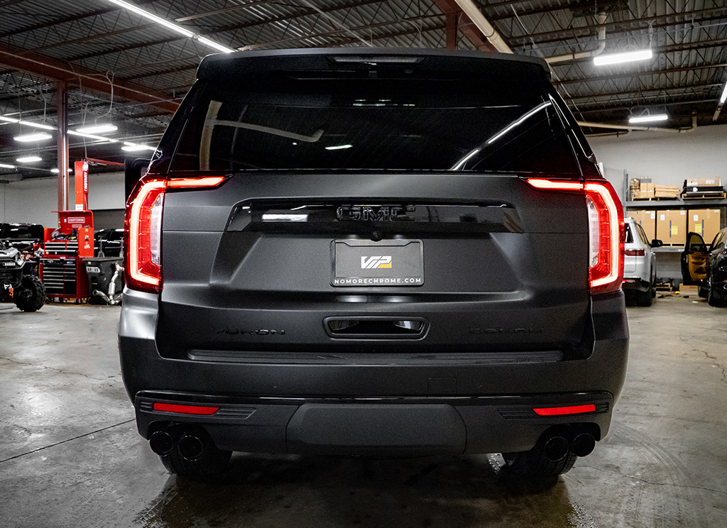 rear view of a blackout GMC Yukon Denali with a chrome delete rear hatch valence, lettering, and bumper accent.