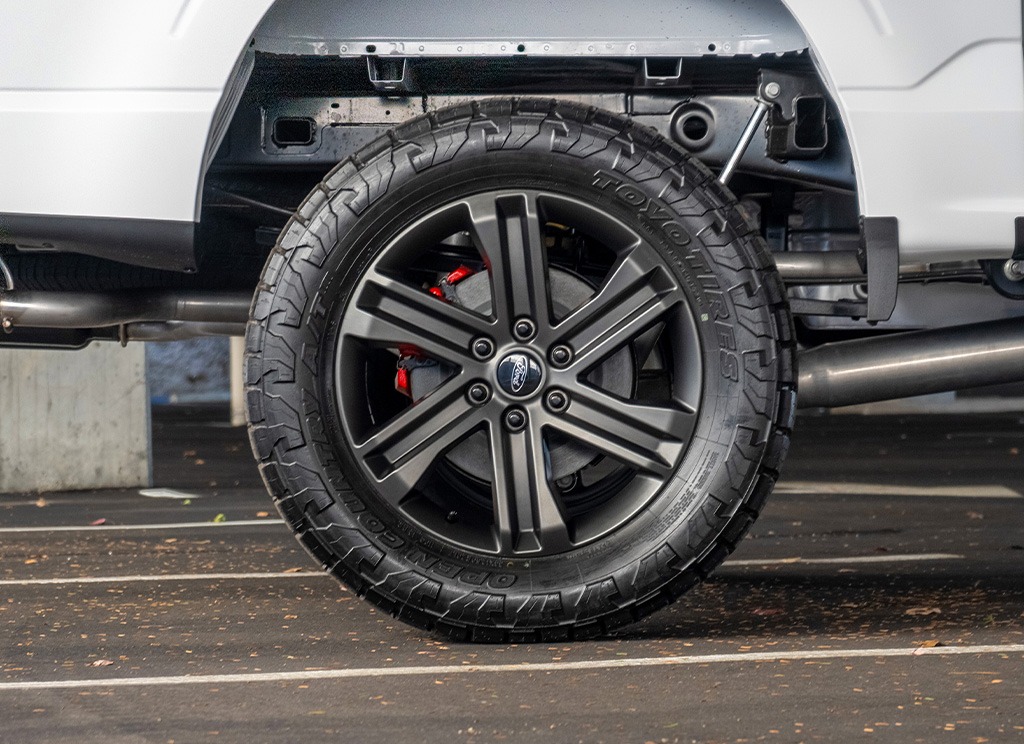 Toyo Open Country AT III tires with red brake calipers on a satin white Ford F-150 pickup truck.