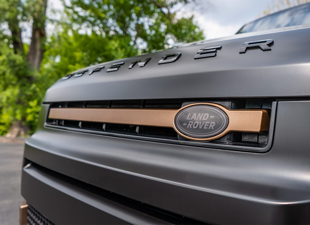 Tinted Land Rover emblem on the grille of a Defender SUV.