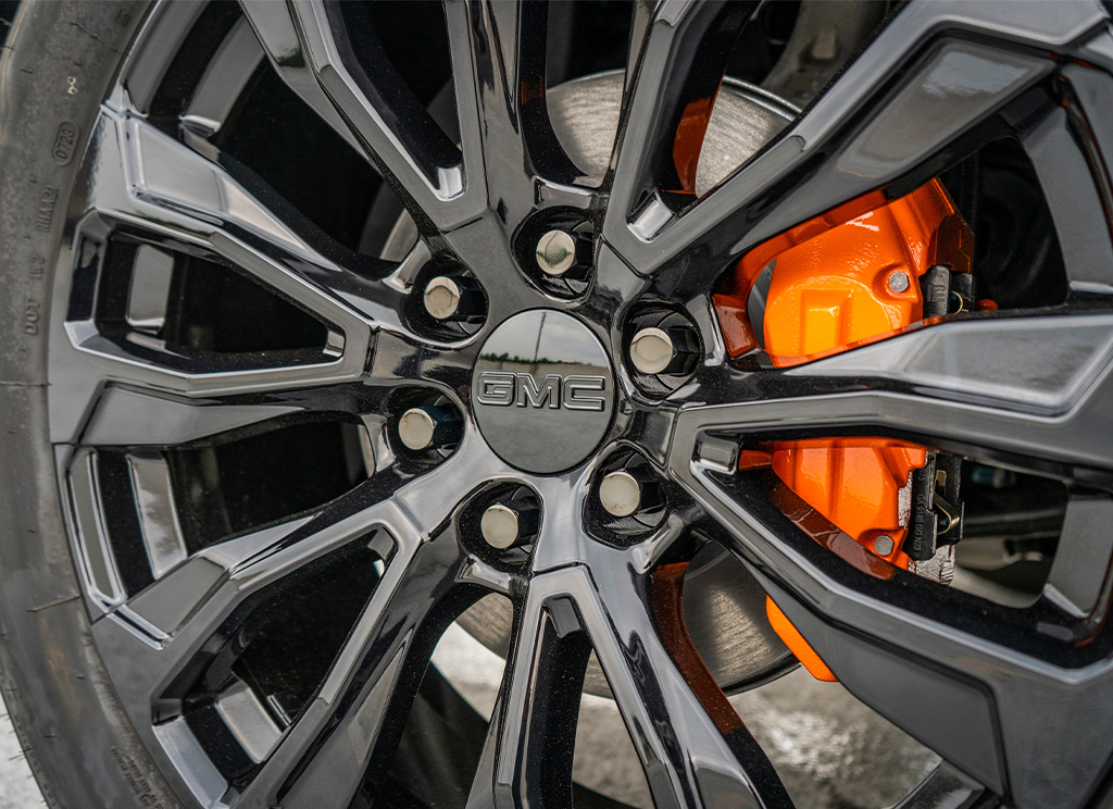 close up of orange painted brake calipers behind black powder coated GMC wheels.