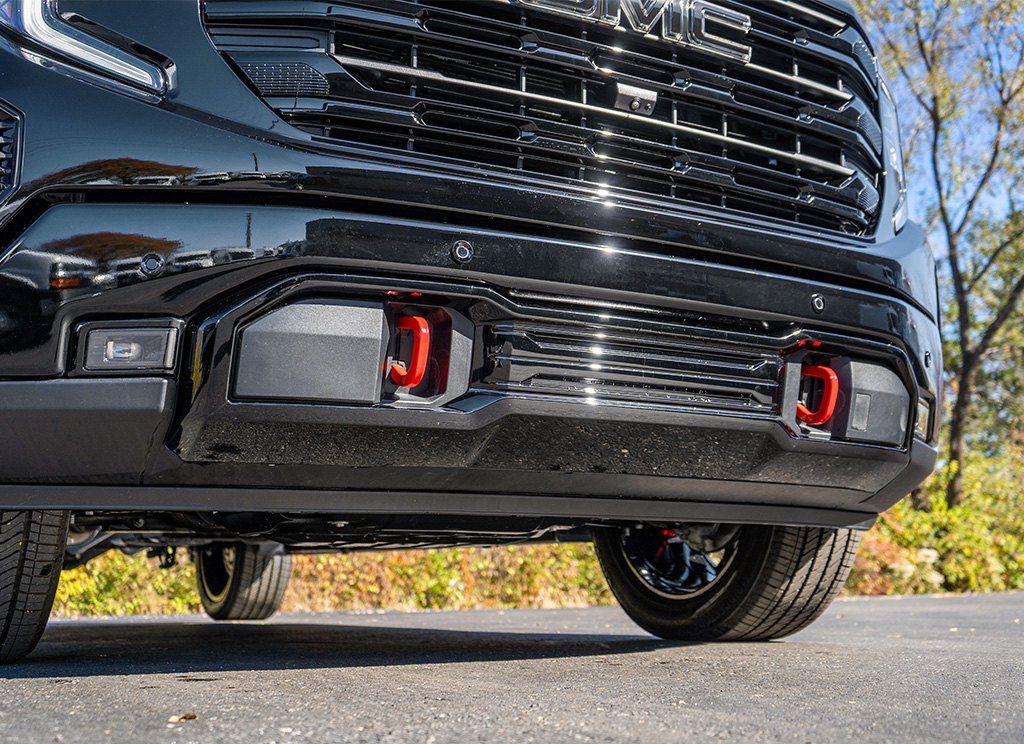 Close up of a 2024 GMC Sierra Denali blackout front bumper accent and red tow hooks.