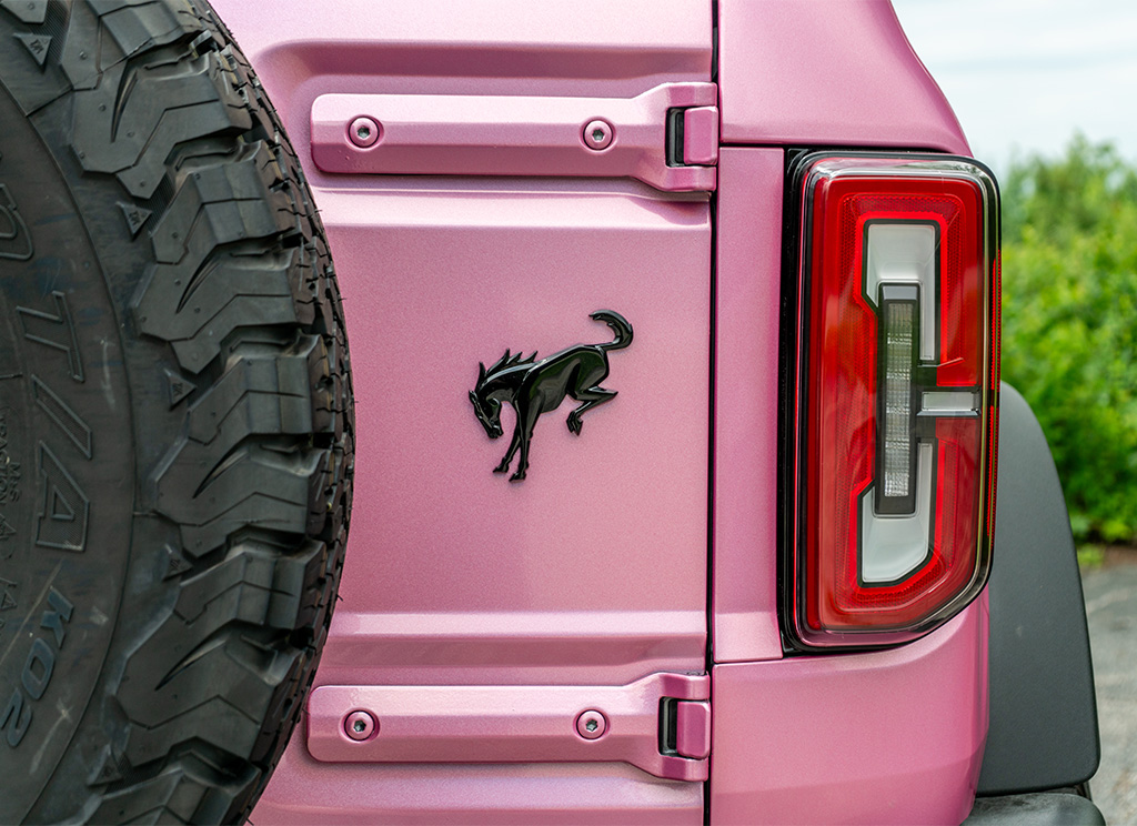 Black Bronco horse emblem on the tailgate of a pink Ford Bronco.