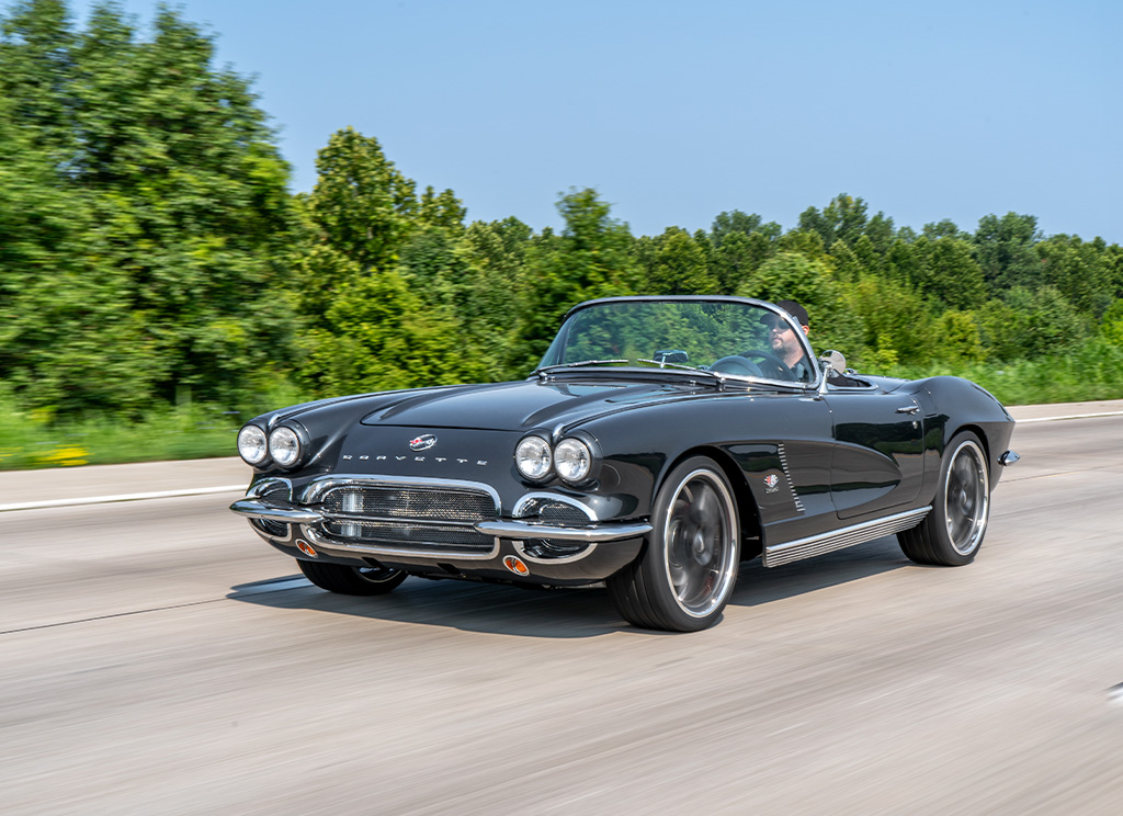 Restored metallic dark grey 1962 C1 Corvette driving on the road.