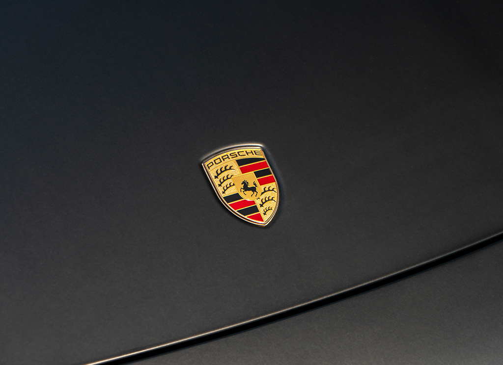 Close-up of the Porsche crest emblem against a matte black vinyl wrapped hood.