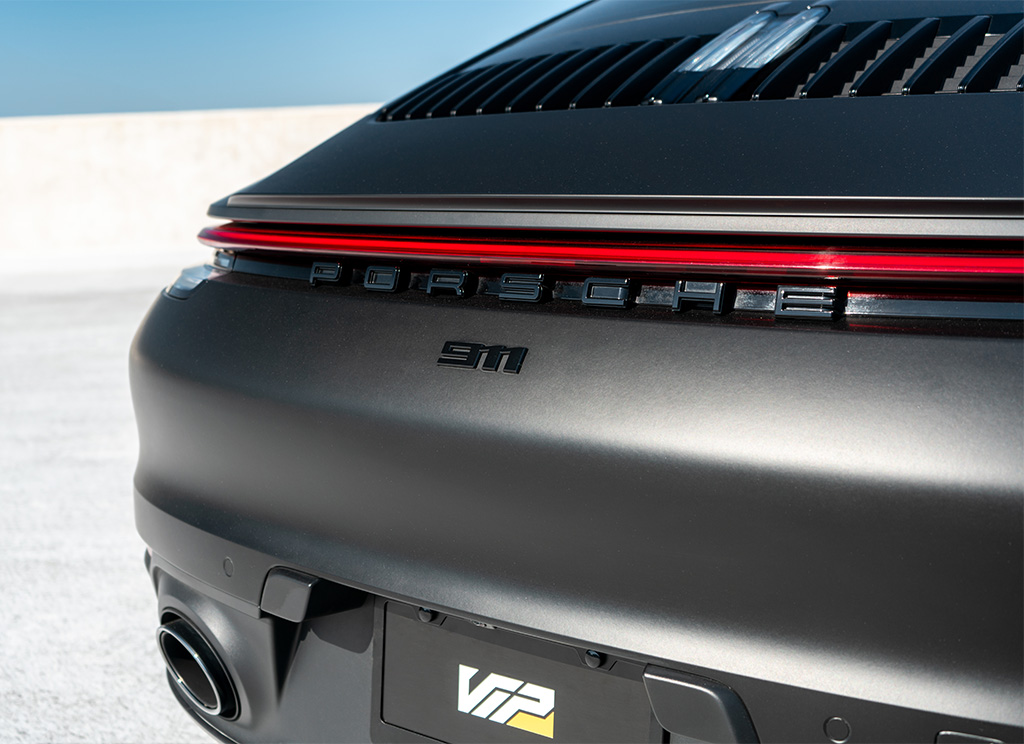 Close-up of the Porsche nameplate on the trunk of a matte black Porsche 911.