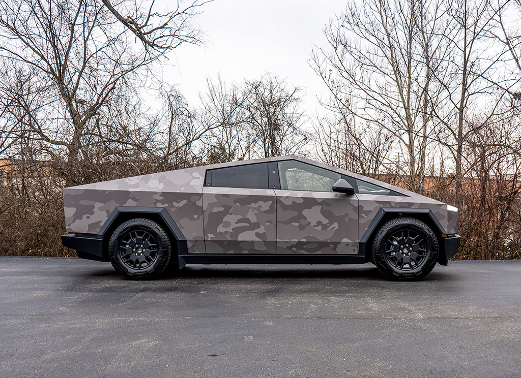 Side profile of a Tesla Cybertruck with a gray camouflage vinyl wrap.