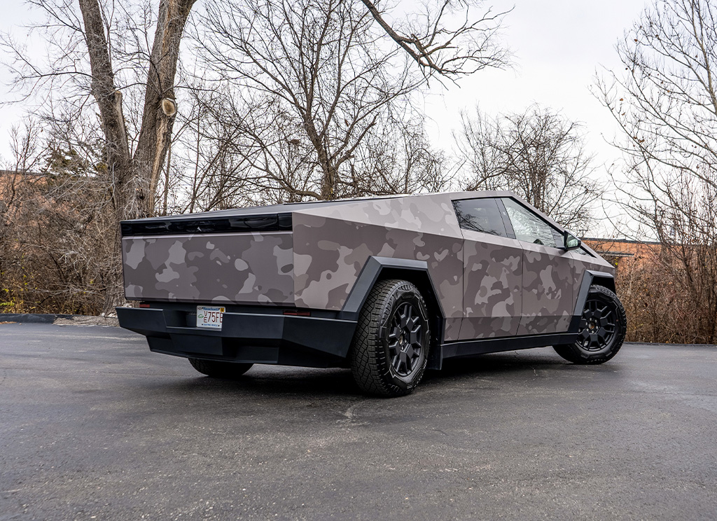 Rear angled view of a Tesla Cybertruck with a custom gray camouflage vinyl wrap.