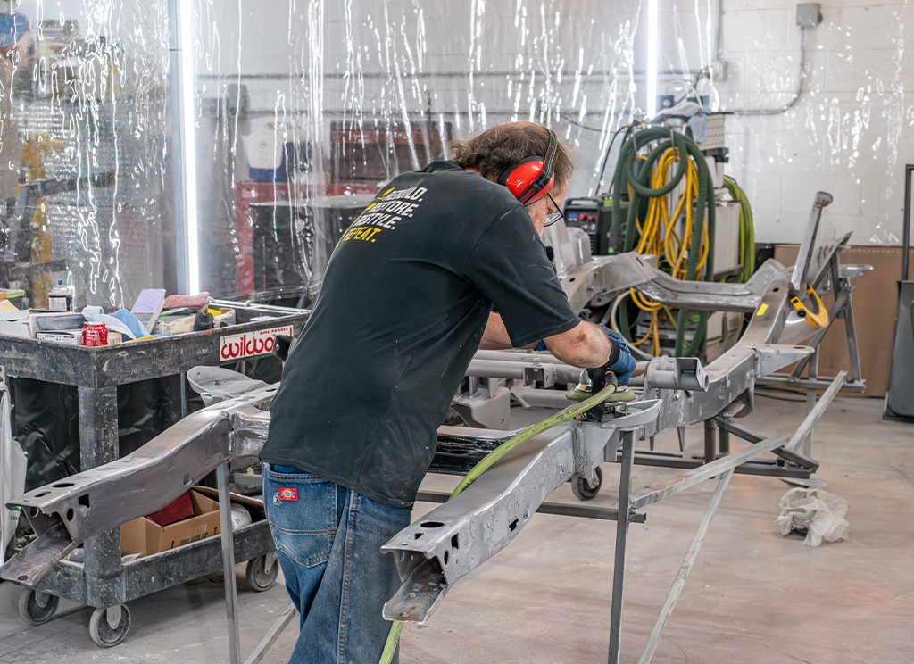 Restoration technician grinding rust off the frame of the chassis.