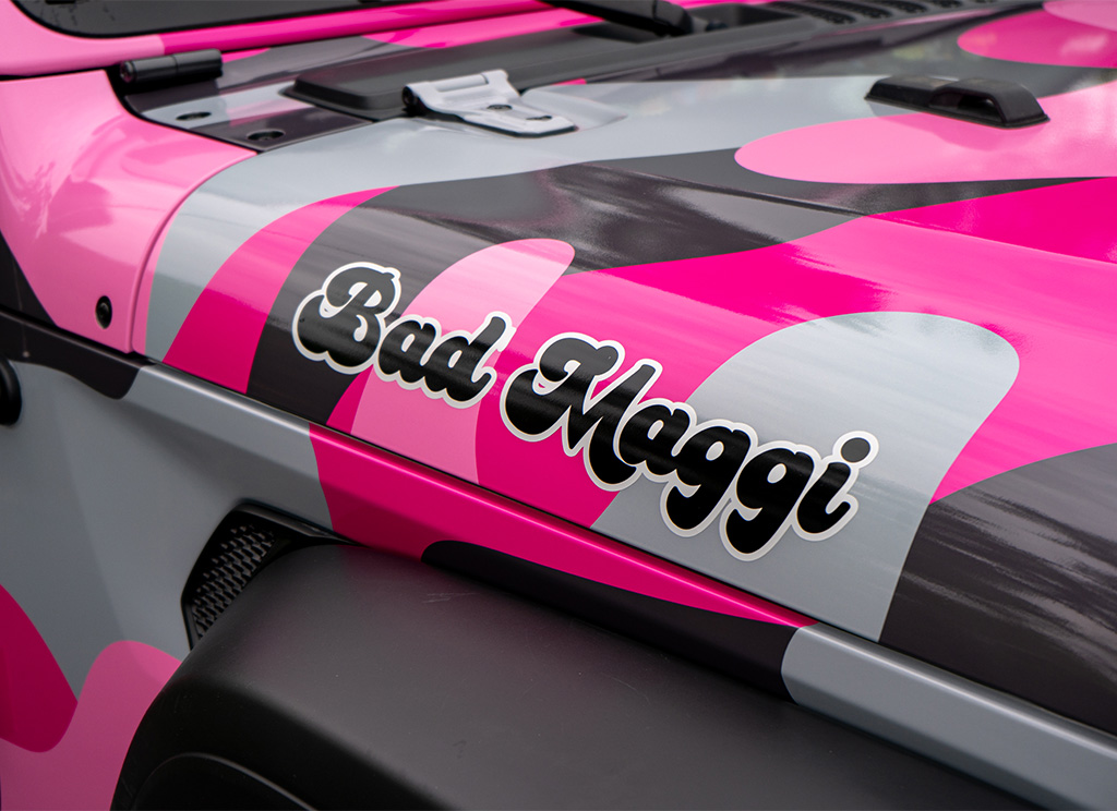 Close-up of a pink camo vinyl wrap and Bad Maggie nameplate sticker.