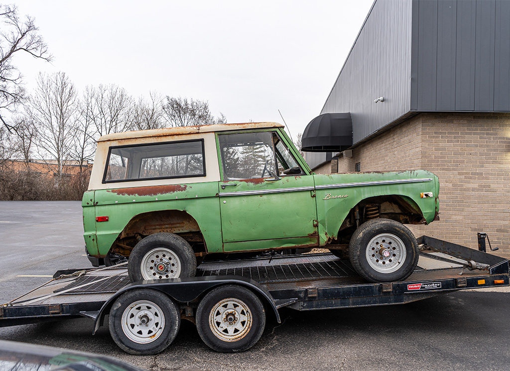 Rusted old Winter Green 1972 Ford Bronco on a trailer side profile view.