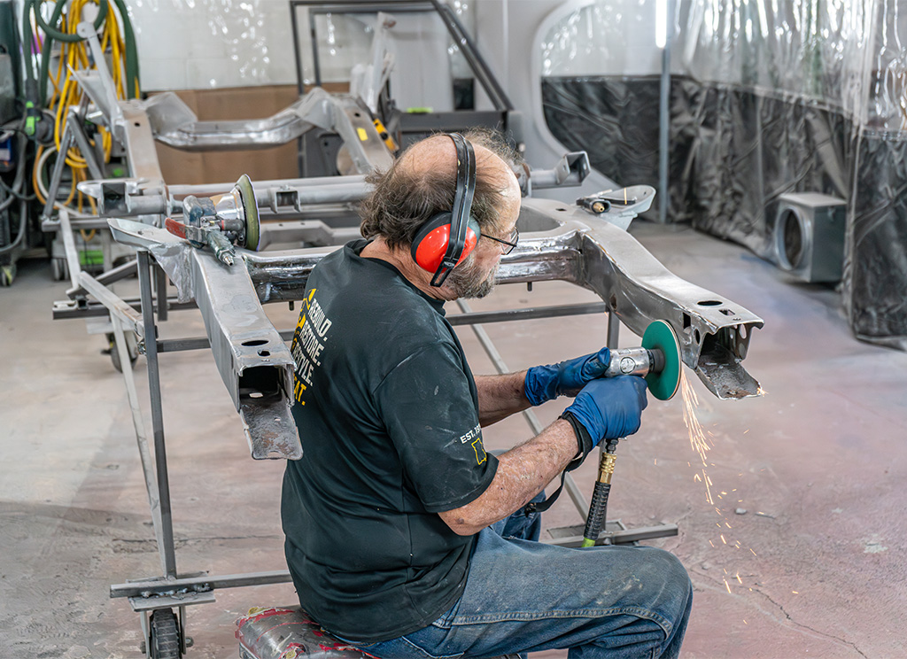 Technician grinding rust off the chassis frame of a restoration build.