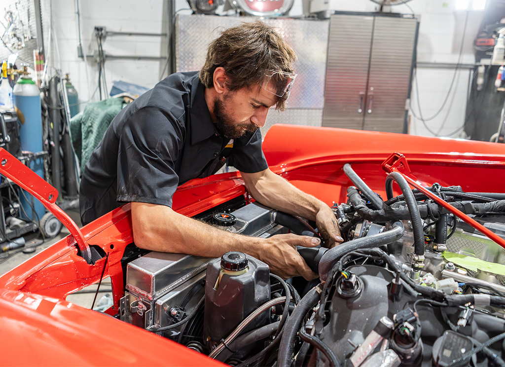 Technician adjusting the cooling system on a red 1956 Ford Thunderbird restoration.