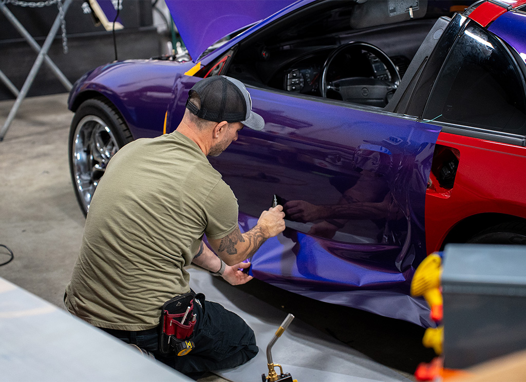 Technician installing iridescent purple vinyl wrap on the driver side door of a 1991 Nissan 300ZX.