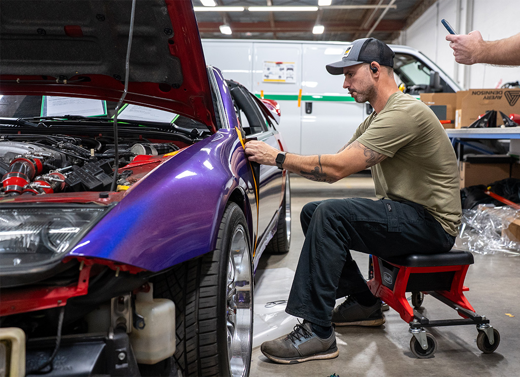 Technician installing iridescent purple vinyl wrap on the fender of a 1991 Nissan 300ZX.