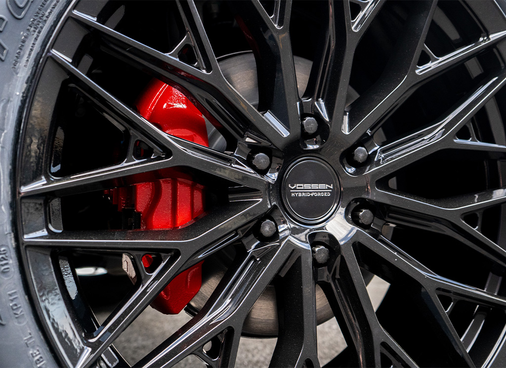 Close-up of red painted brake calipers behind custom gloss black Vossen HFX-6 wheels.