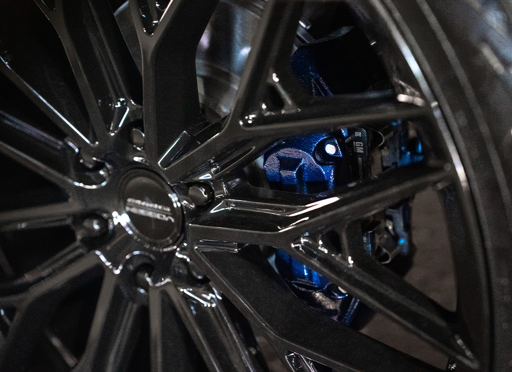 Close-up of a metallic blue brake caliper behind custom gloss black wheels.