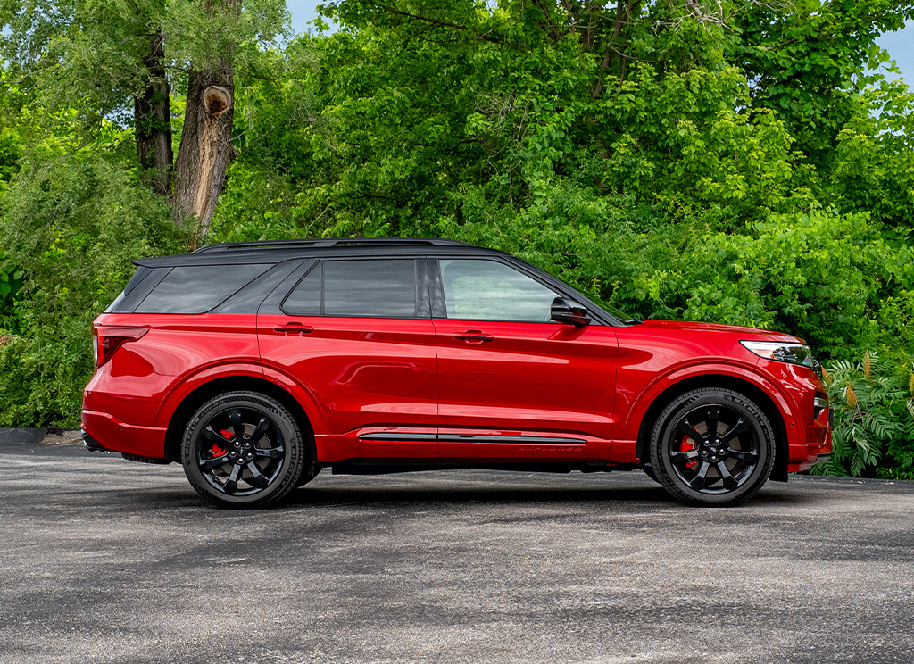 Side profile of a custom red 2022 Ford Explorer that has color-matched cladding and a black roof wrap.